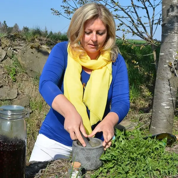 Eunike Grahofer verarbeitet draußen frische Kräuter in einem Mörser